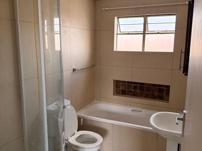 A functional bathroom featuring a shower enclosure, bathtub, pedestal basin, and toilet with neutral wall and floor tiling.
