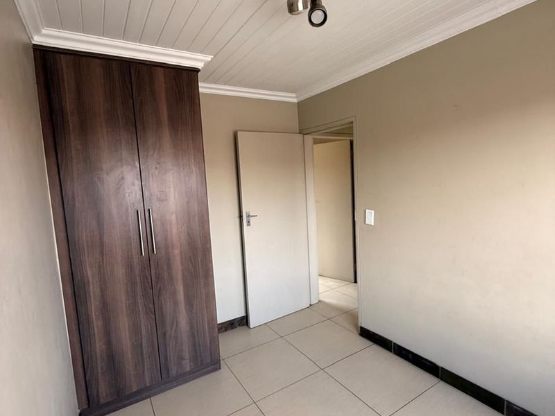A vacant bedroom featuring tiled flooring, a built-in wardrobe, and a tongue and groove ceiling, ready for personalization.
