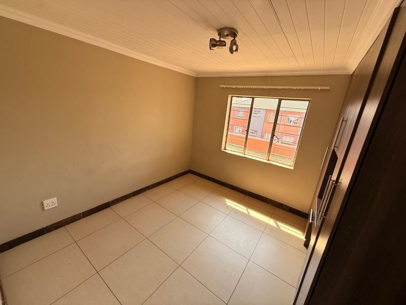 A clean, empty bedroom featuring tiled flooring, a built-in wardrobe, and a tongue and groove ceiling with natural light.