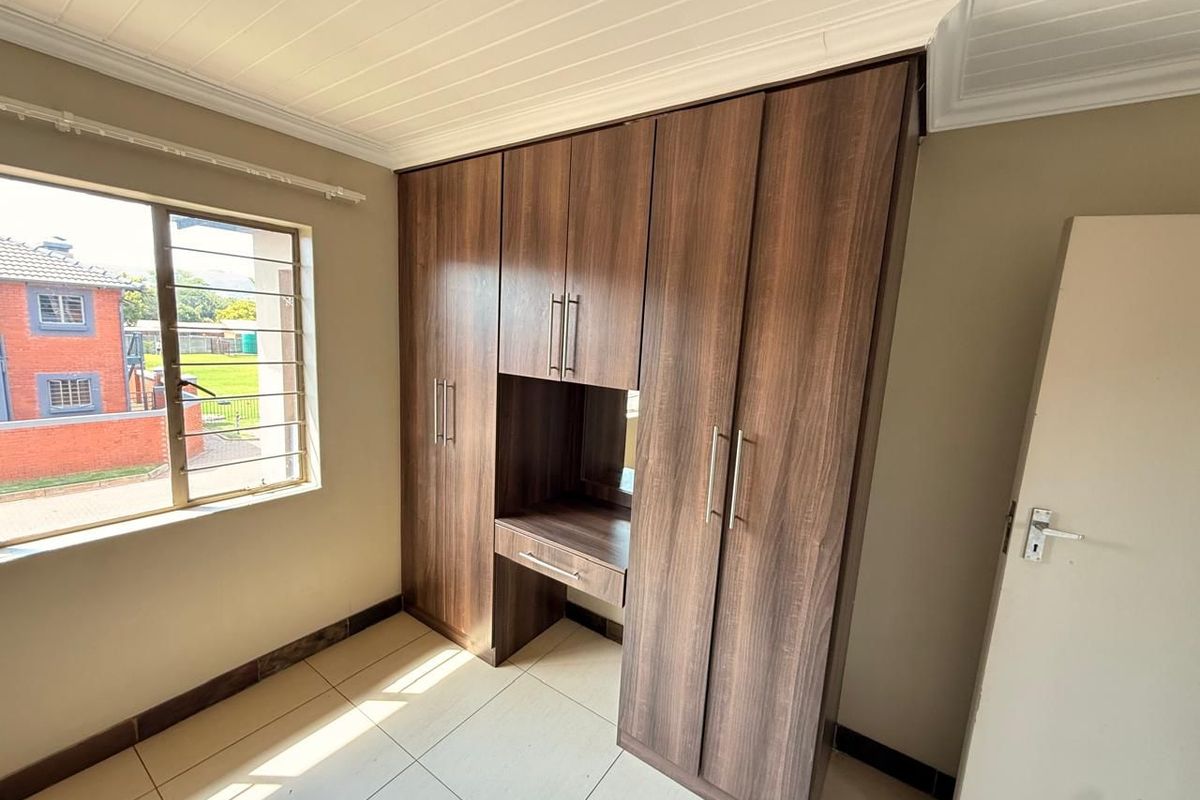 A bright bedroom featuring modern wood-finish built-in cupboards with an integrated vanity, tiled flooring, and a classic tongue and groove ceiling.