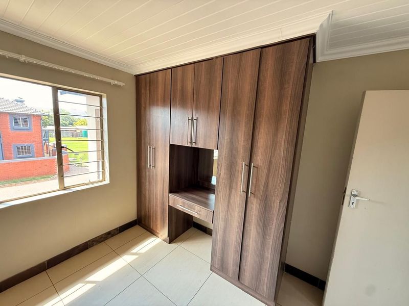 A bright bedroom featuring modern wood-finish built-in cupboards with an integrated vanity, tiled flooring, and a classic tongue and groove ceiling.