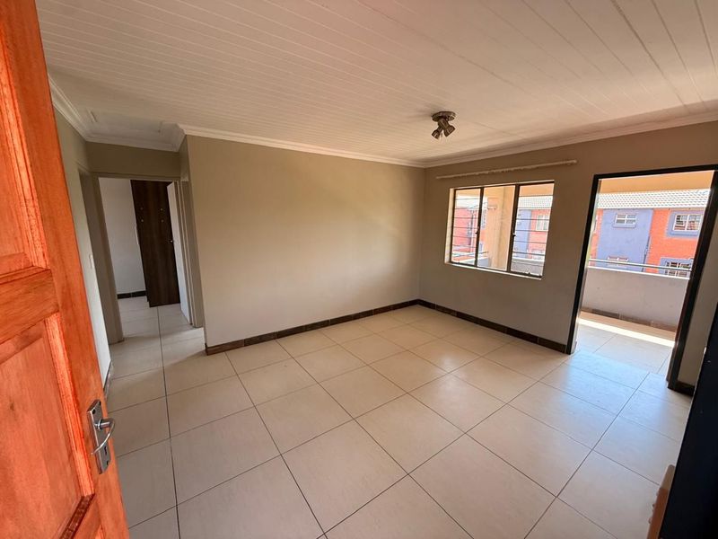 An empty, well-lit living area featuring neutral tiled flooring, a timber-look ceiling, and direct access to an outdoor balcony.