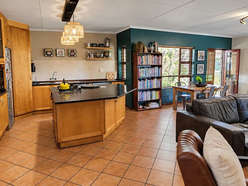 Spacious open-plan living area featuring a well-equipped kitchen with wooden cabinetry, a central island, and tiled flooring throughout, seamlessly connecting to the lounge.