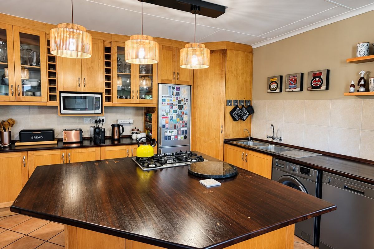A well-equipped kitchen featuring extensive wooden cabinetry, a central island with a gas hob, integrated appliances, and a tiled backsplash.