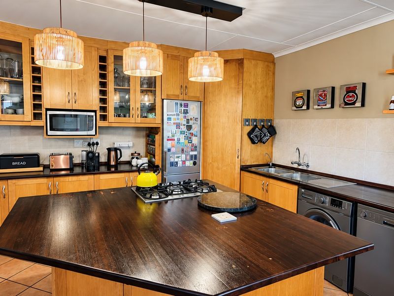A well-equipped kitchen featuring extensive wooden cabinetry, a central island with a gas hob, integrated appliances, and a tiled backsplash.