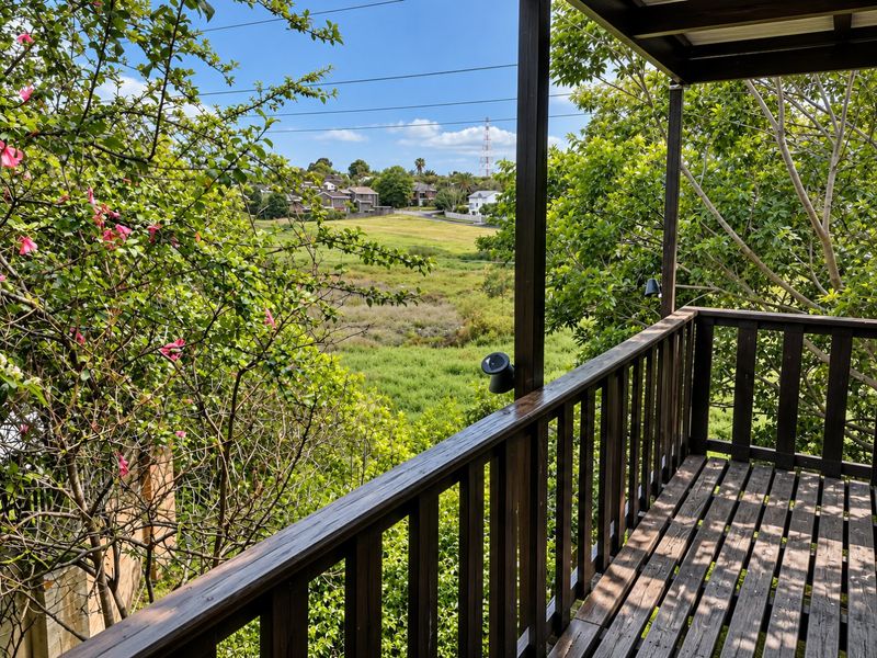 A raised timber balcony featuring a wooden balustrade and overhead cover, offering elevated views over the surrounding landscape and neighborhood.