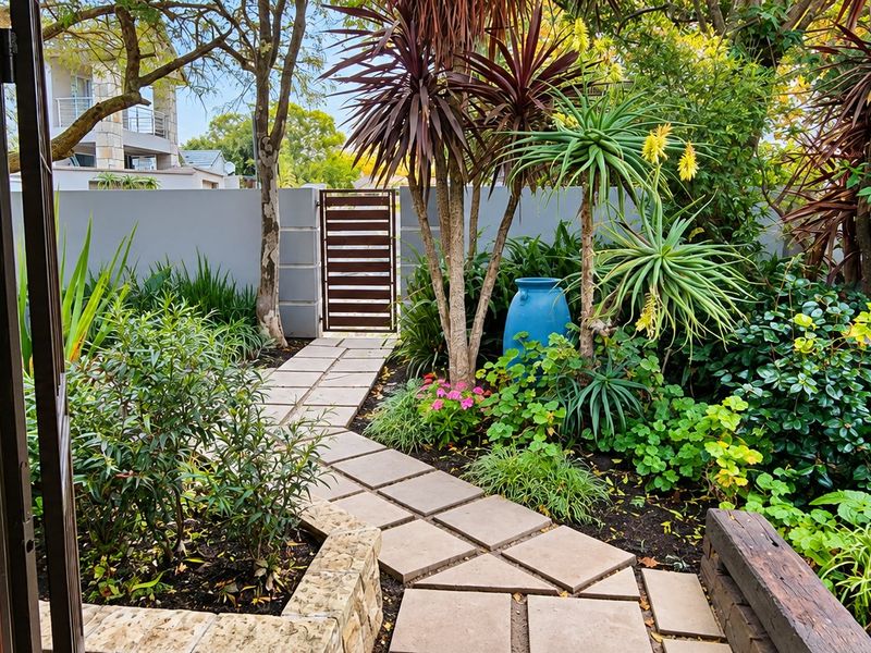 A well-maintained private garden featuring a paved walkway, established landscaping, and a secure pedestrian gate leading to the property boundary.