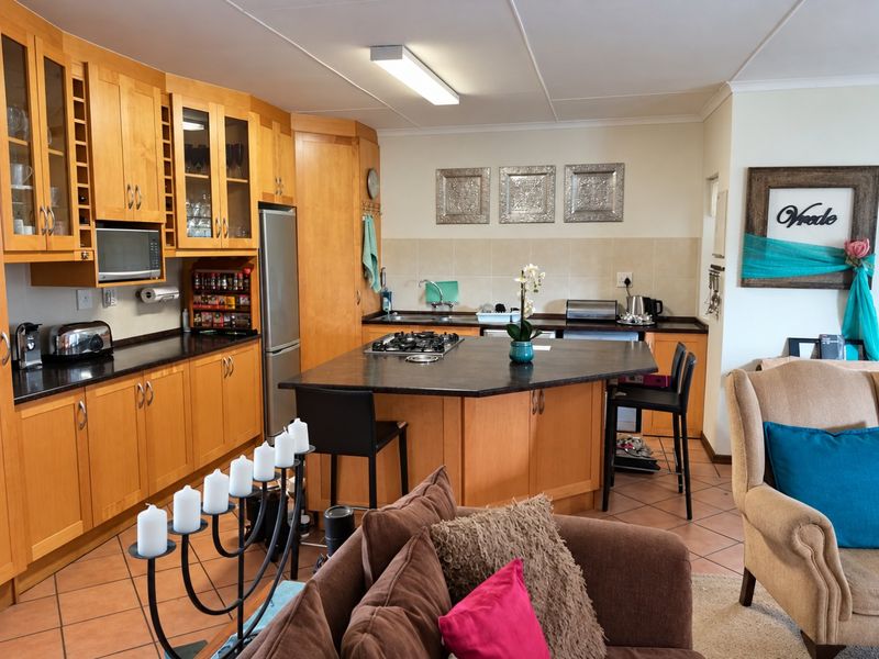 Open plan kitchen featuring wooden cabinetry, a central island with a gas hob, and tiled flooring, seamlessly integrated with the living area.