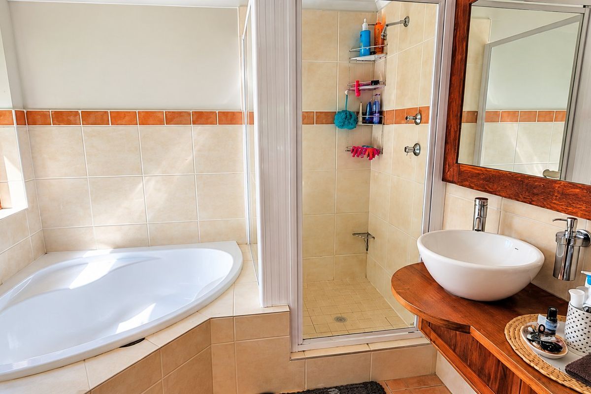 A bright bathroom featuring a corner bathtub, a separate walk-in shower, and a wooden vanity with a vessel sink, overlooking lush greenery.