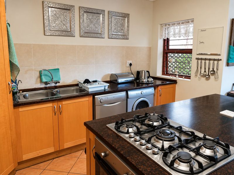 Functional kitchen featuring wooden cabinetry, granite countertops, a built-in gas hob, oven, and double sink with tiled backsplash and flooring.