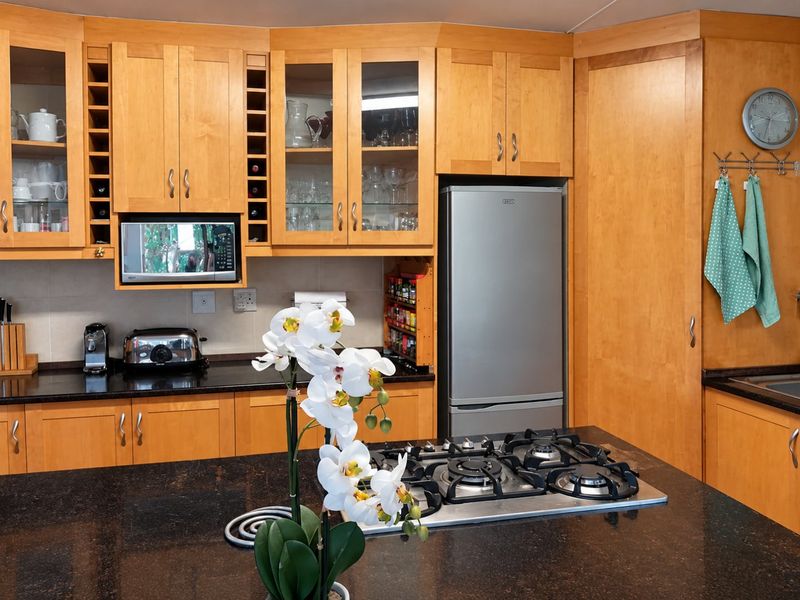 A well-maintained kitchen featuring warm wood cabinetry, granite countertops, a central island with a gas hob, and integrated storage solutions.