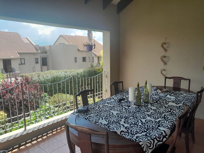 A covered balcony featuring tiled flooring, exposed timber rafters, and a wrought iron balustrade, offering an open-air space for outdoor dining.