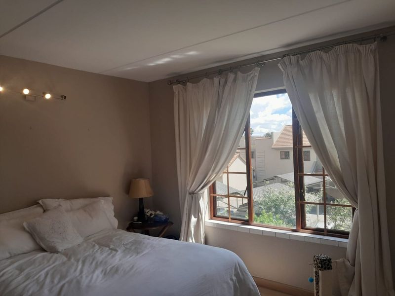 A bedroom featuring wooden window frames, a tiled window sill, and neutral wall tones, offering a view of the surrounding residential complex.