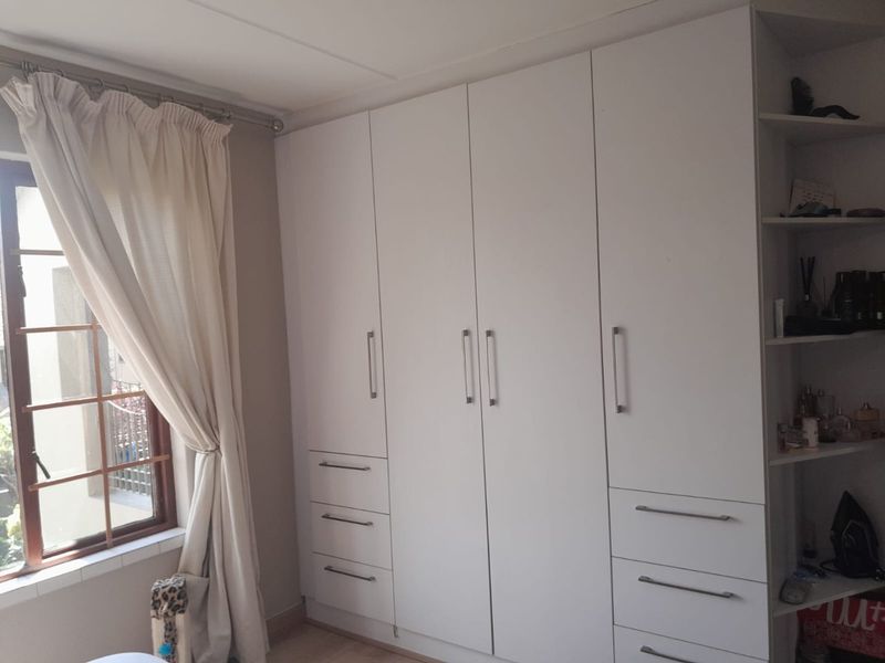 A bedroom featuring white built-in cupboards with integrated drawers and adjacent open shelving, providing ample storage space.
