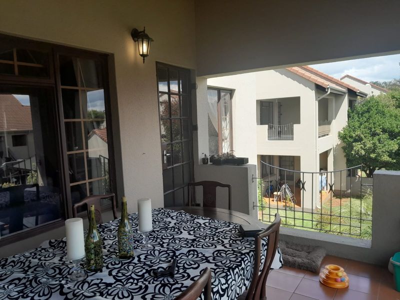 A covered balcony featuring tiled flooring, a wall-mounted light fixture, and a metal balustrade, offering an outdoor space overlooking the complex grounds.