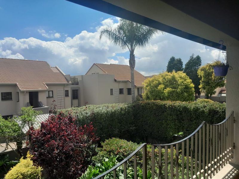 A view from a balcony overlooking a landscaped garden and neighboring residential units under a bright sky.
