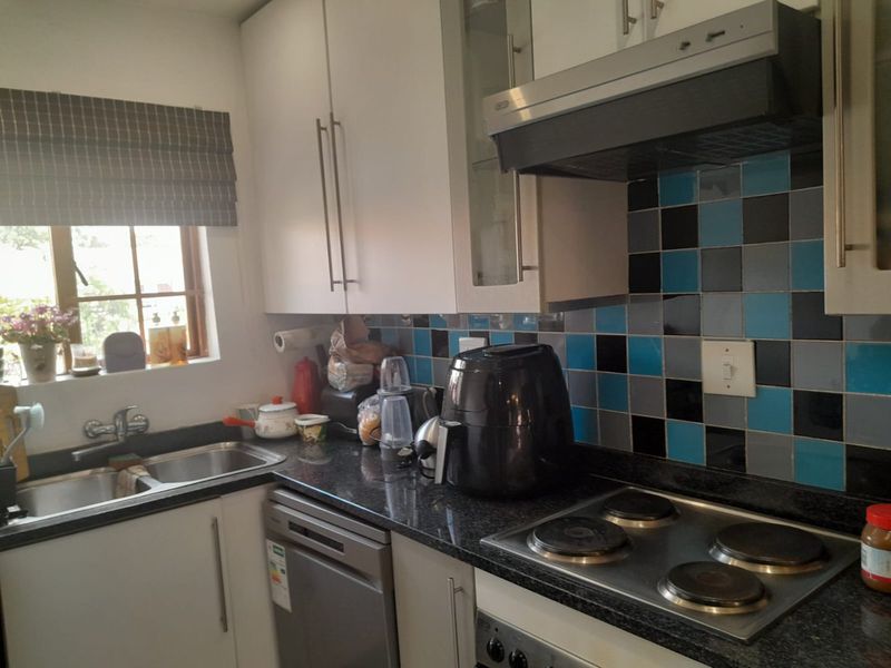 A functional kitchen featuring white cabinetry, dark granite countertops, a tiled backsplash, and integrated appliances including an electric hob and extractor fan.