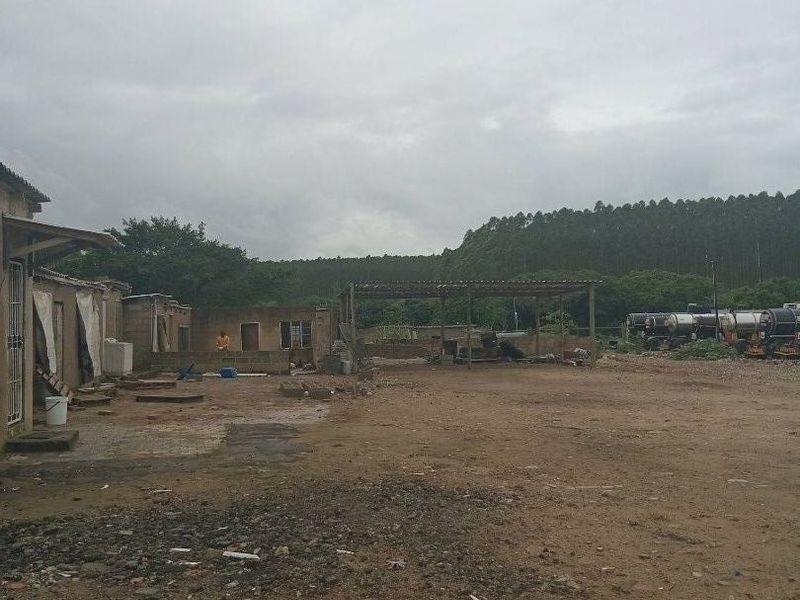 An expansive, unpaved rear yard area featuring a basic masonry building shell and an open-sided shed structure under an overcast sky.