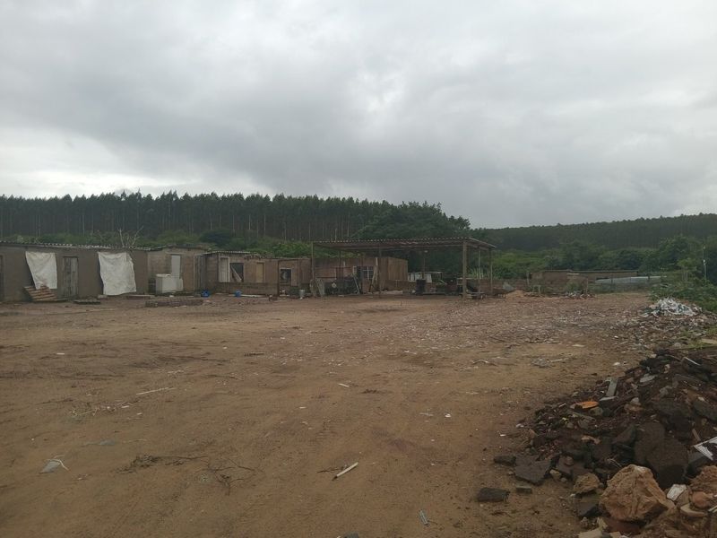 A large, unpaved outdoor area featuring a basic covered structure and several small, weathered outbuildings in need of significant maintenance.