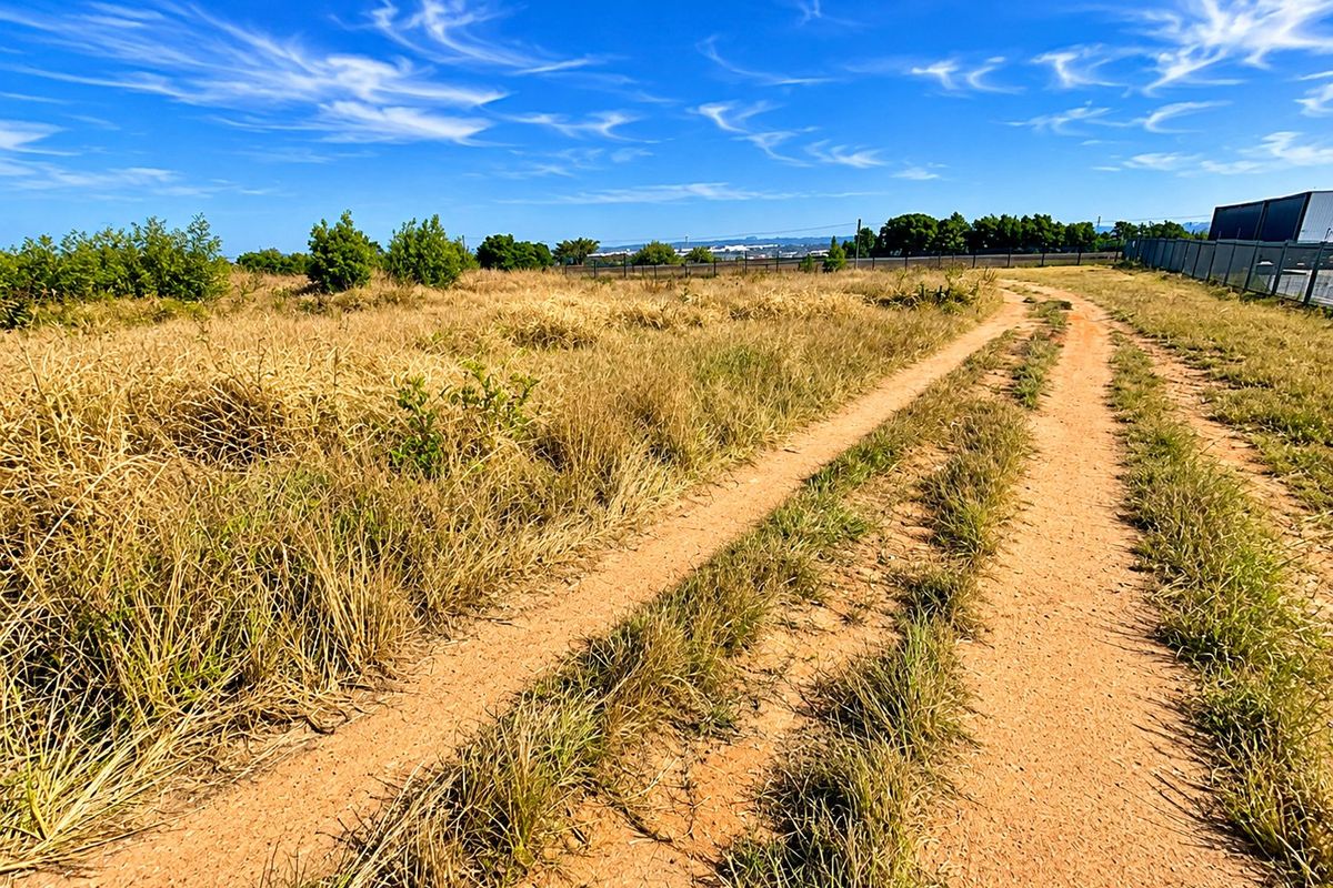 A view of a vacant residential plot featuring a dirt access track and perimeter fencing under a clear blue sky.