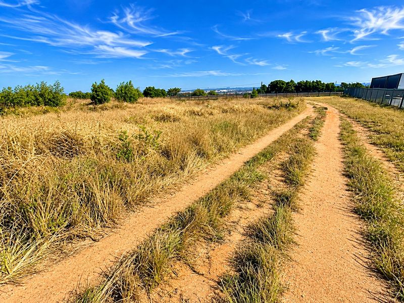 A view of a vacant residential plot featuring a dirt access track and perimeter fencing under a clear blue sky.