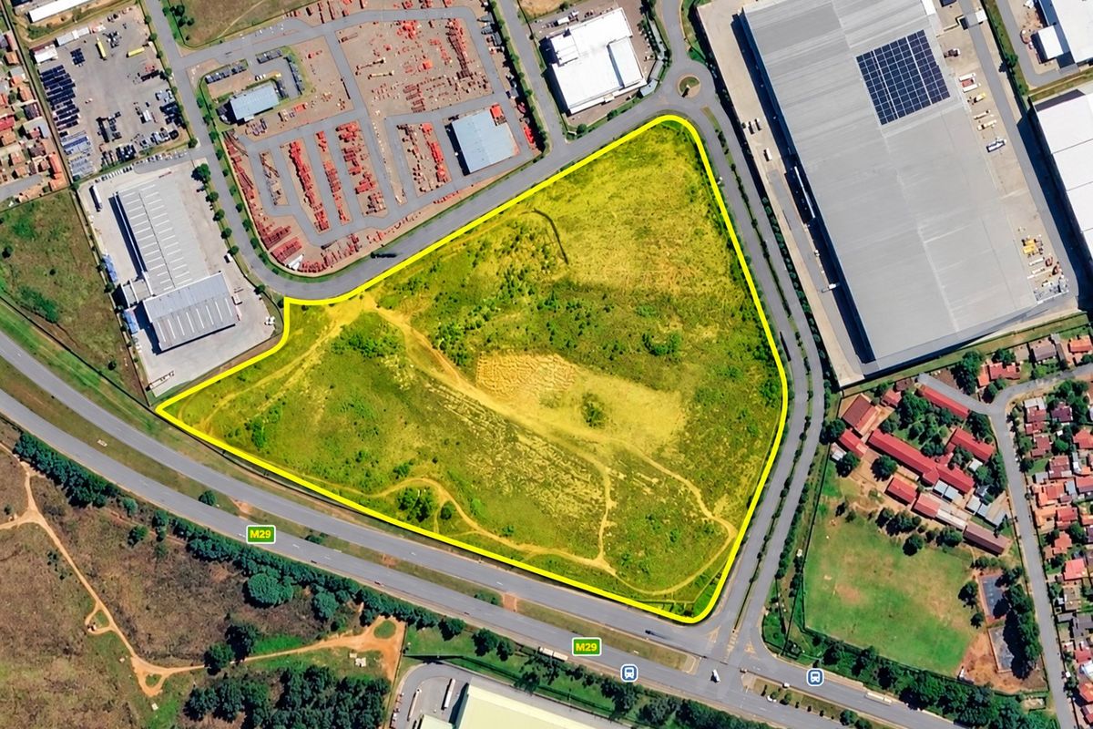 An aerial view of a large, triangular-shaped vacant residential plot situated near major roads and commercial infrastructure.