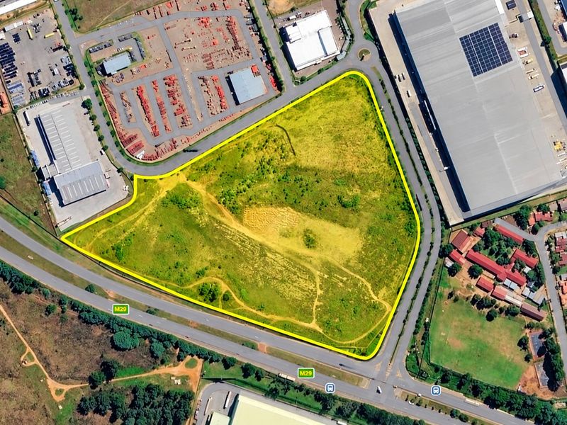 An aerial view of a large, triangular-shaped vacant residential plot situated near major roads and commercial infrastructure.