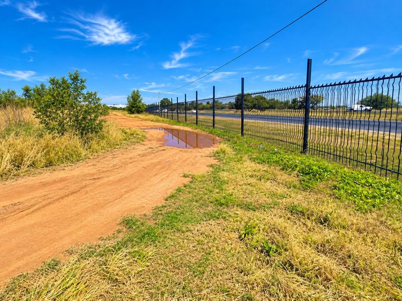A vacant residential plot featuring a dirt access track, metal security fencing along the boundary, and overhead power lines.