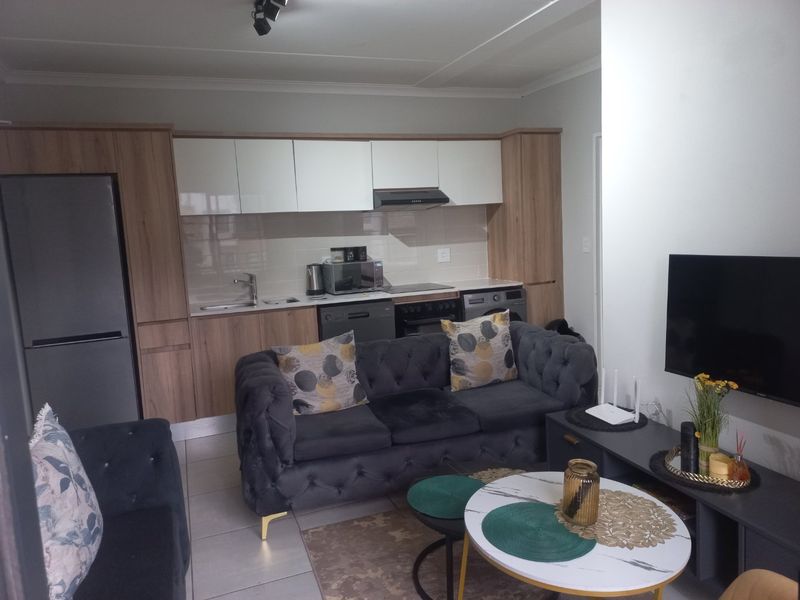 Modern open-plan living area featuring a contemporary kitchen with built-in cabinetry, integrated appliances, and tiled flooring, seamlessly connected to the lounge space.