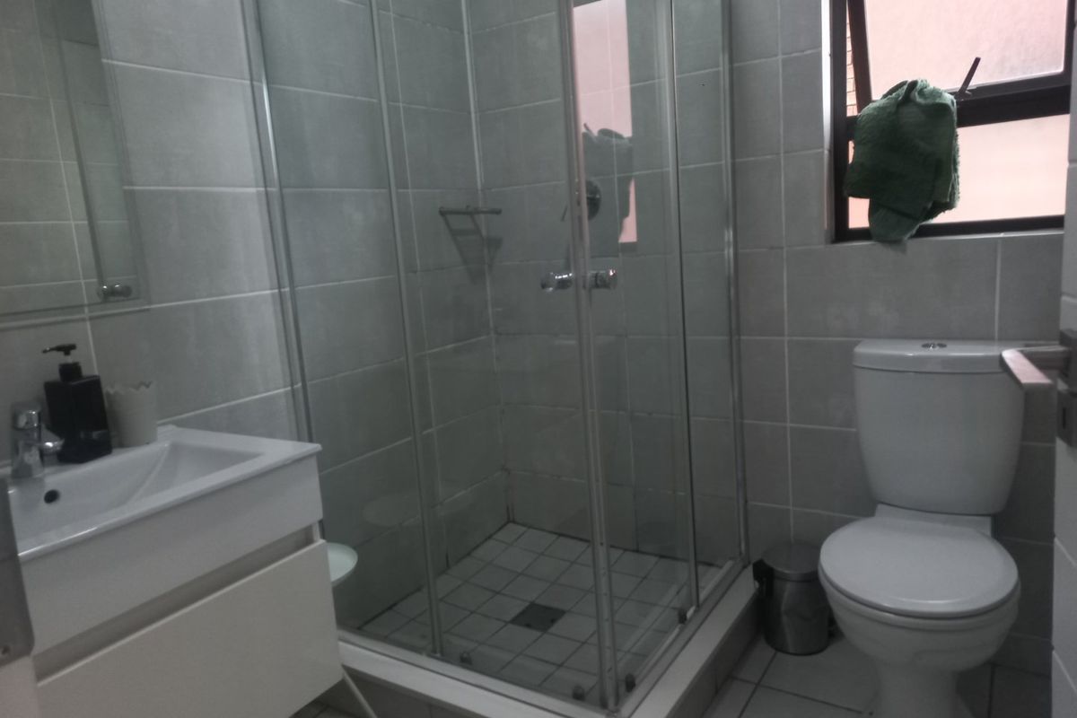 A functional bathroom featuring a glass shower enclosure, a modern vanity basin, and a standard toilet with neutral wall and floor tiling.