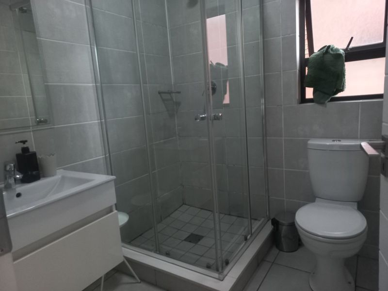 A functional bathroom featuring a glass shower enclosure, a modern vanity basin, and a standard toilet with neutral wall and floor tiling.