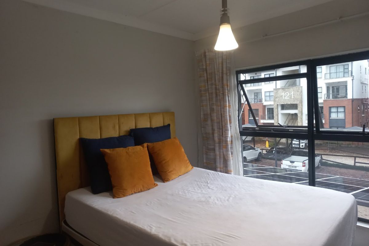 A bedroom featuring a large window with views of the complex, neutral walls, and a central pendant light fixture.