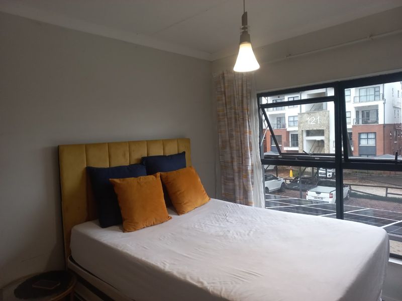 A bedroom featuring a large window with views of the complex, neutral walls, and a central pendant light fixture.