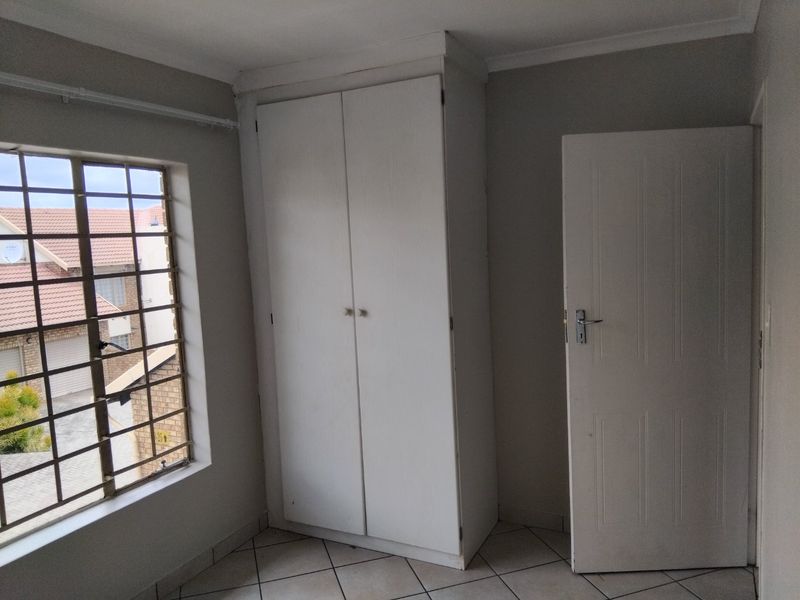 A clean, empty bedroom featuring tiled flooring, a built-in wardrobe, and a window fitted with security bars.
