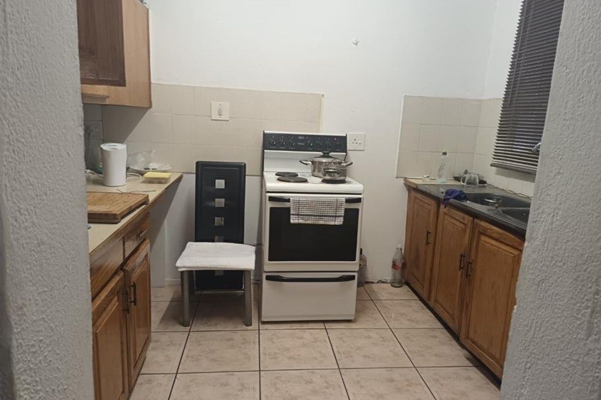 A functional kitchen featuring wooden cabinetry, a freestanding stove, tiled splashbacks, and tiled flooring, offering potential for modernization and aesthetic updates.