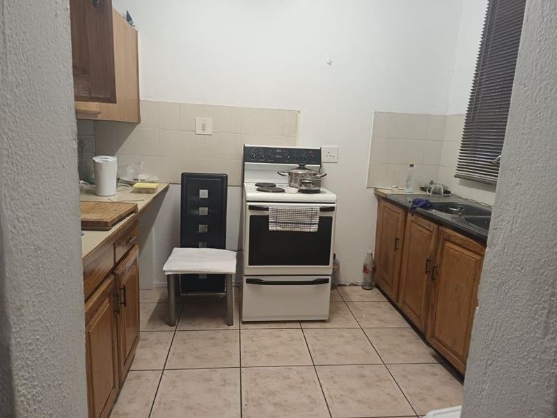 A functional kitchen featuring wooden cabinetry, a freestanding stove, tiled splashbacks, and tiled flooring, offering potential for modernization and aesthetic updates.