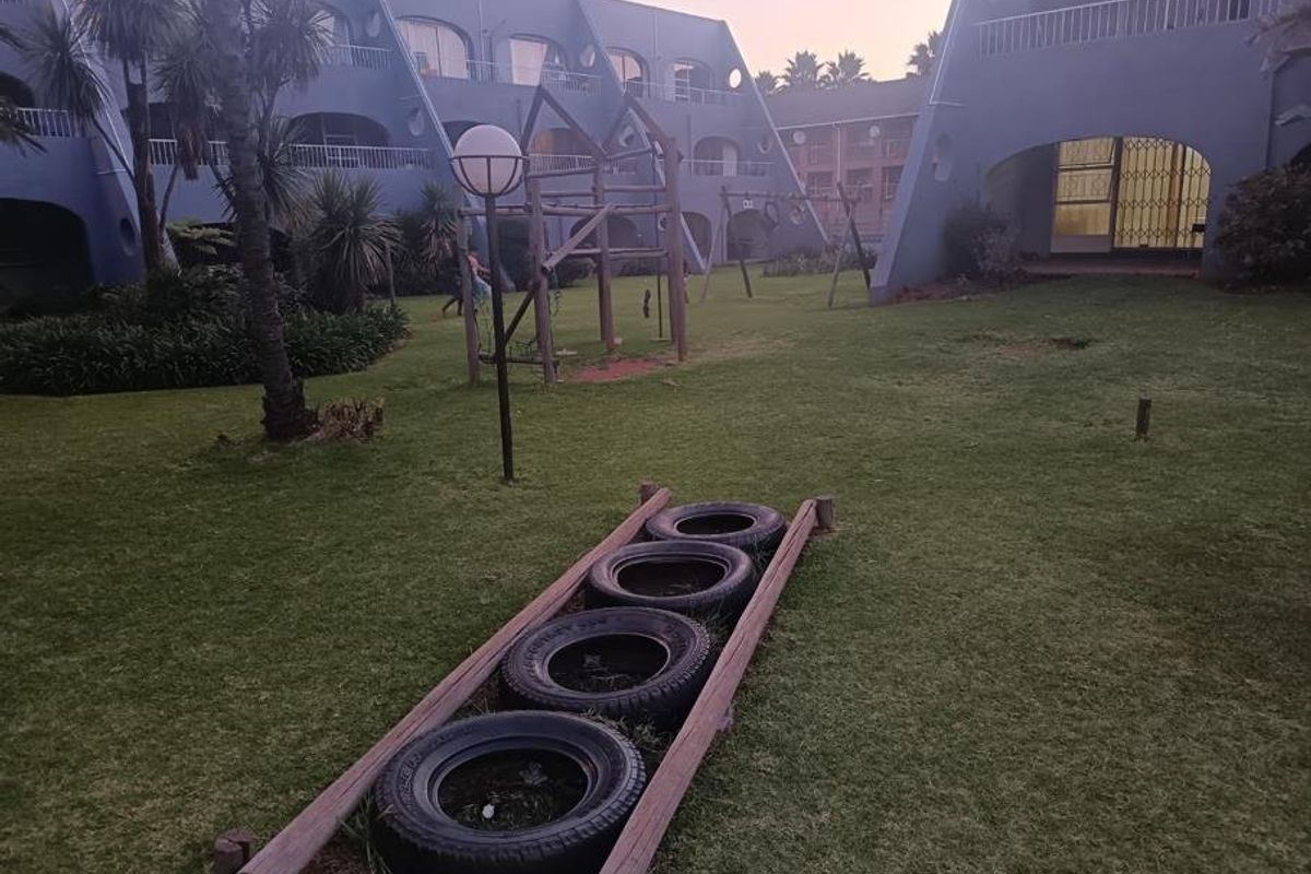 A view of the communal garden area featuring a playground and landscaped grounds between apartment building blocks.