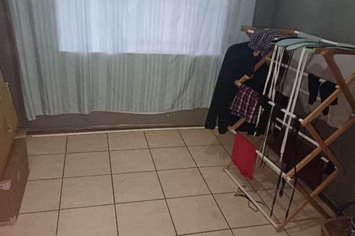 A sparsely furnished bedroom featuring tiled flooring and a large window with curtains, requiring minor cosmetic updates to improve its overall appeal.