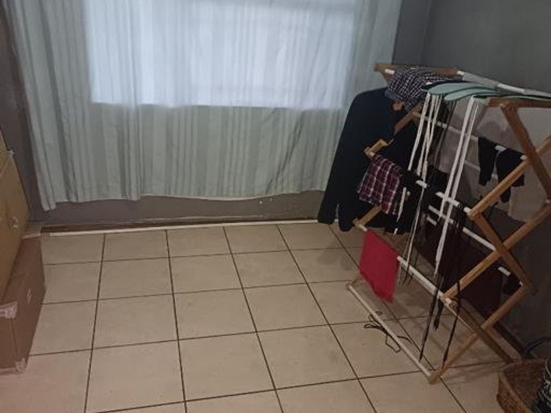 A sparsely furnished bedroom featuring tiled flooring and a large window with curtains, requiring minor cosmetic updates to improve its overall appeal.