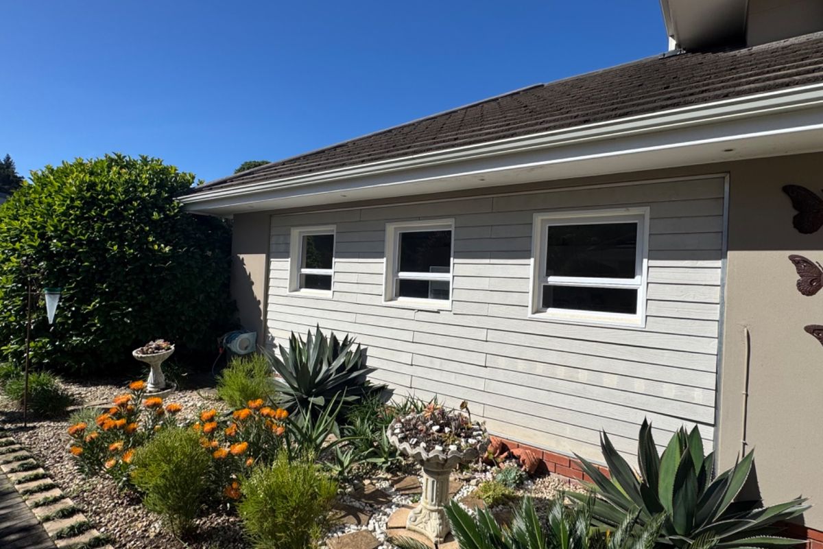 A well-maintained rear exterior view of the property featuring weatherboard cladding, tiled roofing, and established garden landscaping.