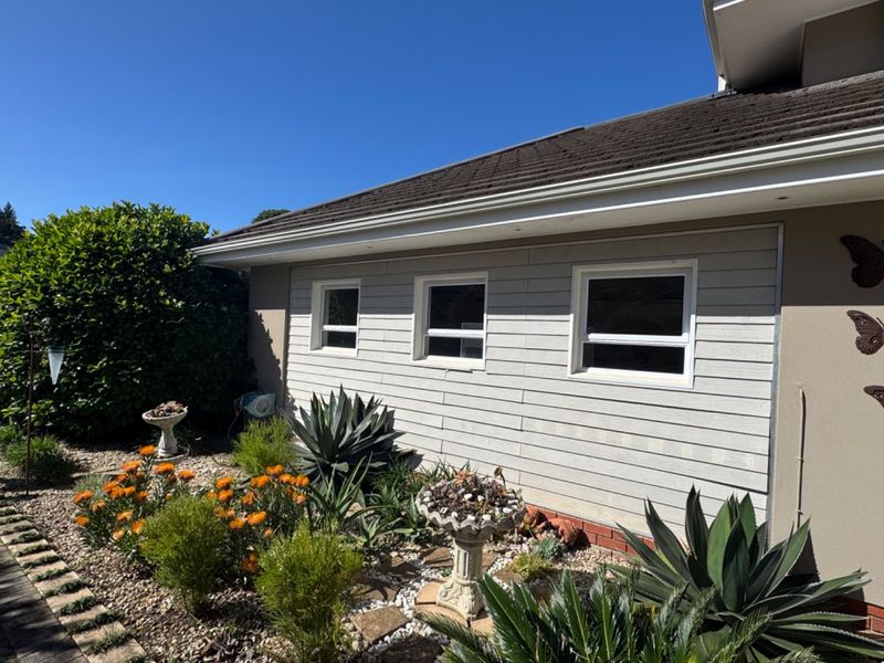 A well-maintained rear exterior view of the property featuring weatherboard cladding, tiled roofing, and established garden landscaping.