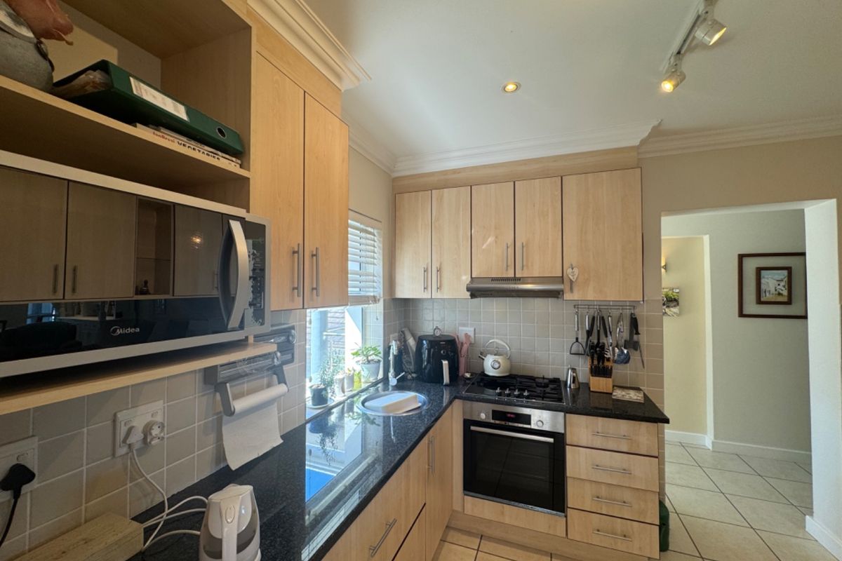 A functional kitchen featuring light wood cabinetry, granite countertops, a gas hob, built-in oven, and tiled backsplash with neutral ceramic flooring.