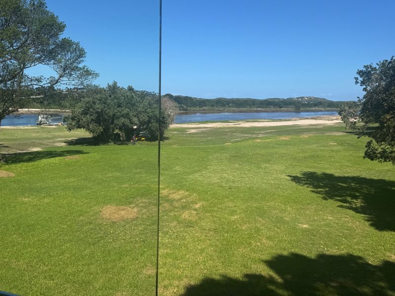A scenic view overlooking a lush green lawn, river, and natural landscape, captured from inside the property.