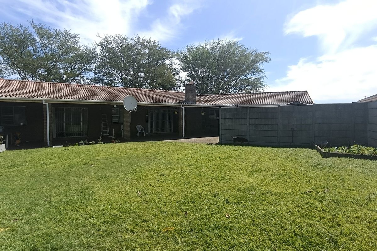 Rear view of the property featuring a brick facade, tiled roof, paved patio area, and a spacious grass garden enclosed by precast concrete walls.