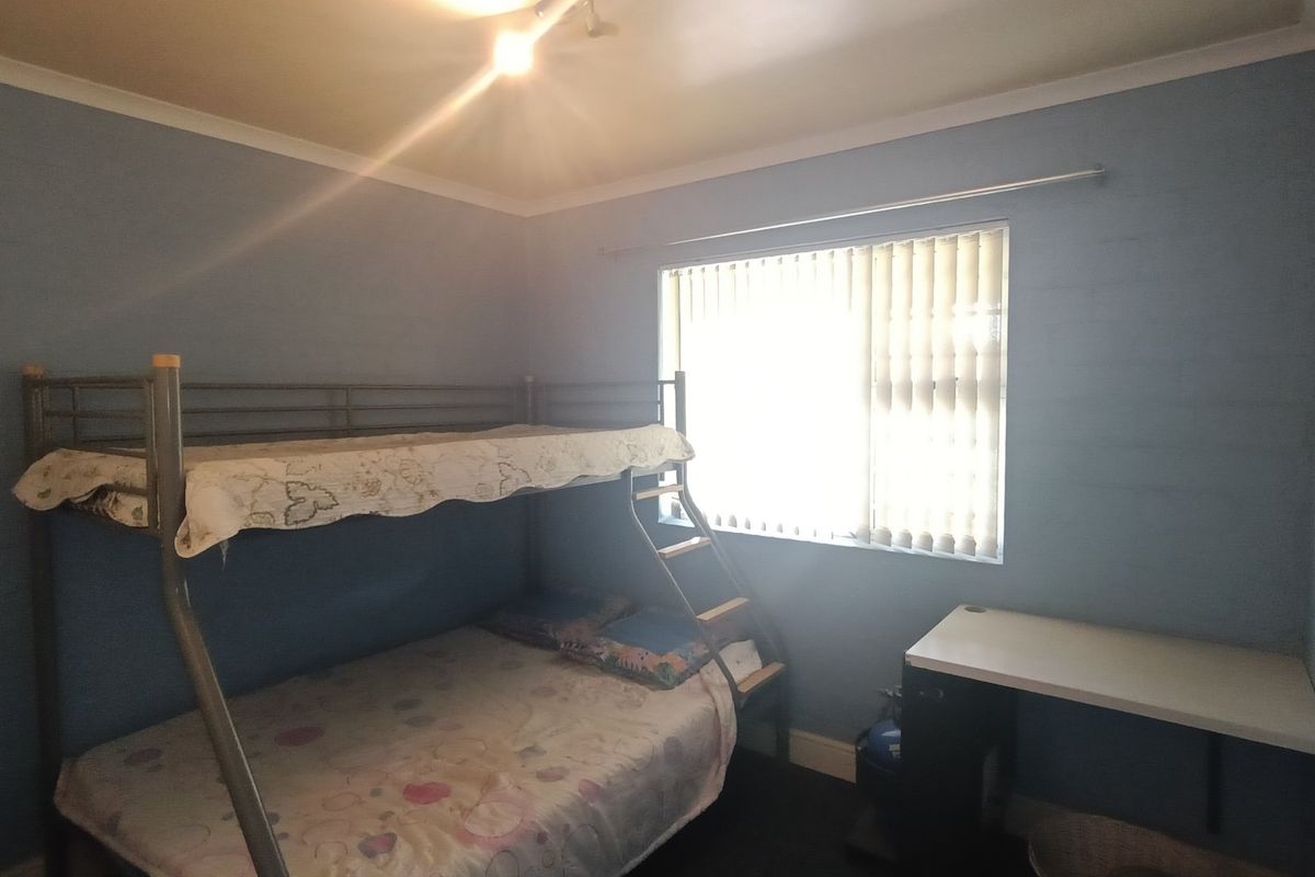 A functional bedroom featuring blue painted walls, a window with vertical blinds, and a wall-mounted desk.