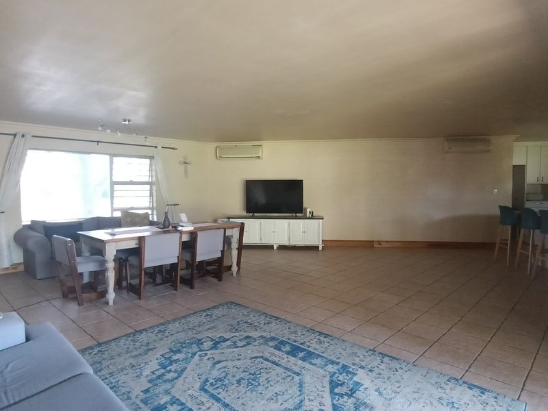 Spacious open-plan living and dining area featuring tiled flooring, dual air conditioning units, and an integrated kitchen with a breakfast bar.