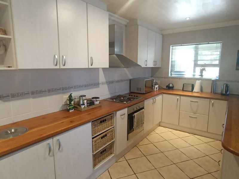 A functional kitchen featuring white cabinetry, warm wooden countertops, a built-in oven and hob, and tiled flooring with a practical layout.