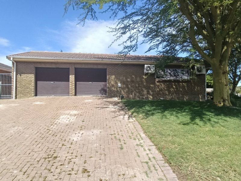 Front view of a brick house featuring a double garage, paved driveway, and established garden area.