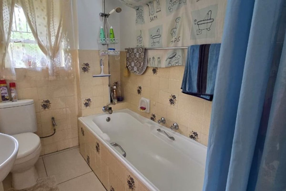 A dated bathroom featuring a bathtub with shower attachment, pedestal sink, and toilet, finished with vintage floral-patterned ceramic wall tiles.