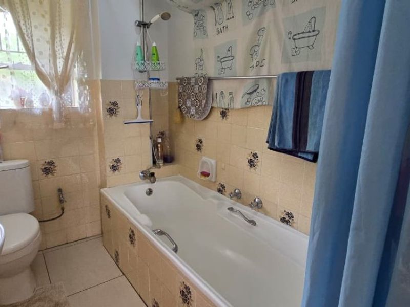 A dated bathroom featuring a bathtub with shower attachment, pedestal sink, and toilet, finished with vintage floral-patterned ceramic wall tiles.